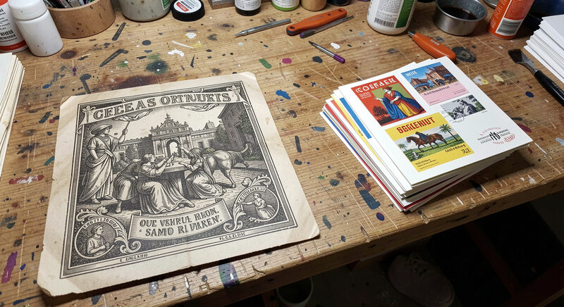 A vintage lithographic printing plate and a stack of coloured postcards on a workshop bench.